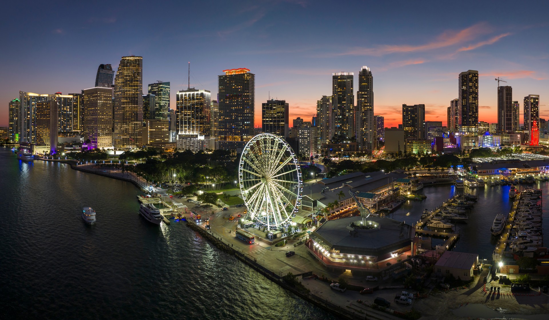 High illuminated skyscrapers of Brickell, city's financial center. Skyviews Miami Observation Wheel at Bayside Marketplace with reflections in Biscayne Bay water and US urban landscape at night